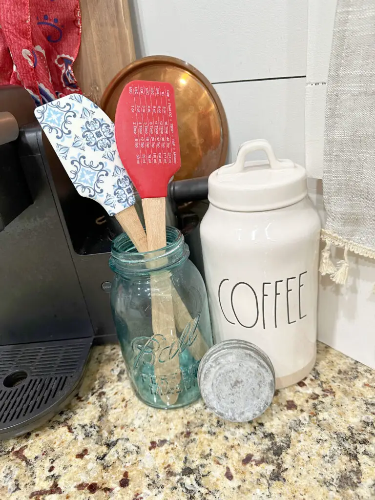 close up of a blue mason jar, red and white and blue kitchen utensils, a white jar that says coffee. 