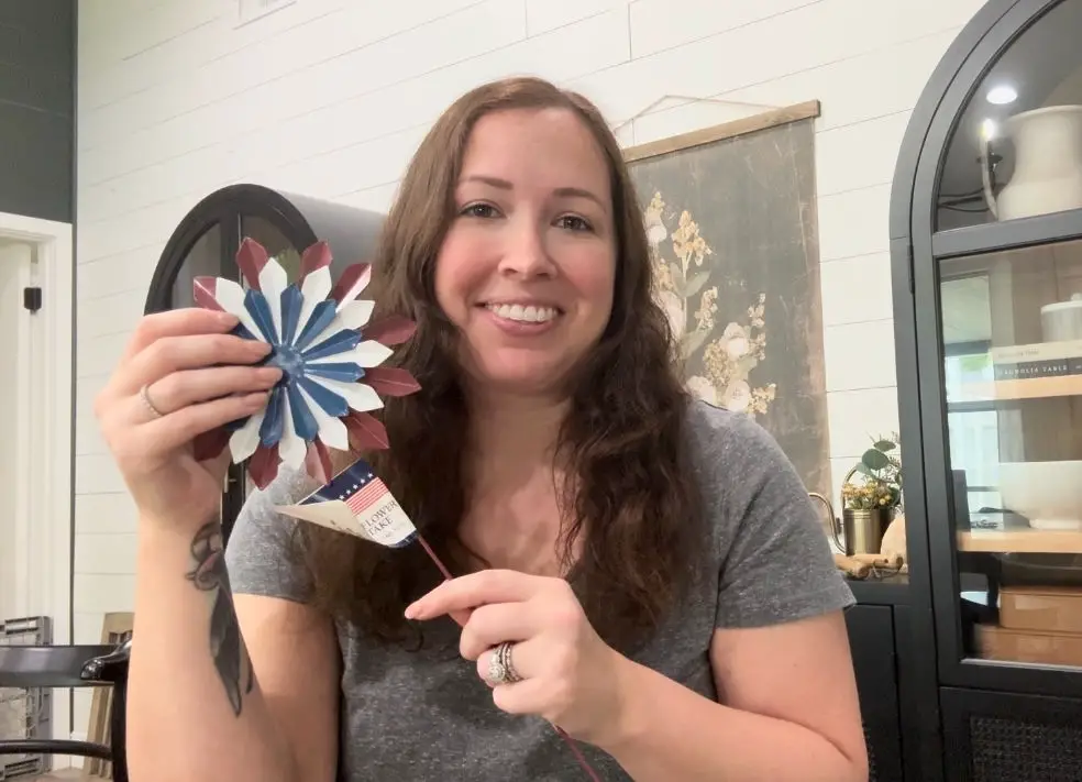 a woman with brown hair holding up a red white and blue firework garden stake.