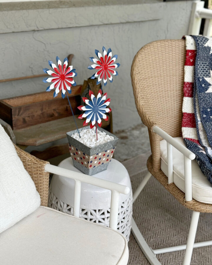 close up of red white and blue firework flowers in a silver vase on a white table, next to rocking chairs