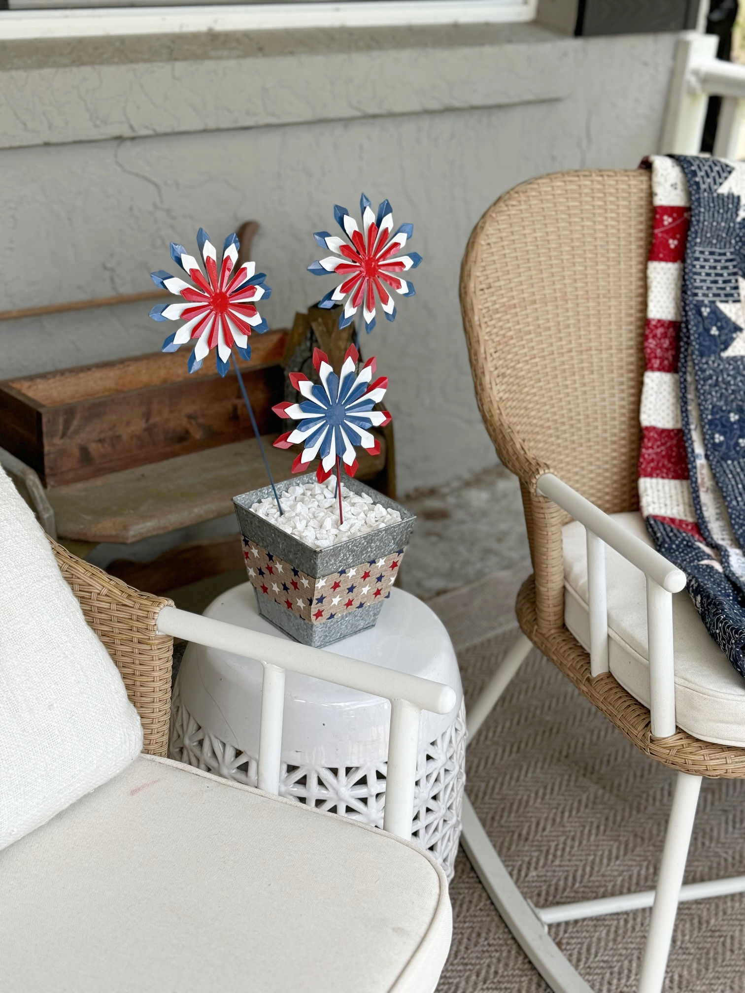 close up of red white and blue firework flowers in a silver vase on a white table, next to rocking chairs